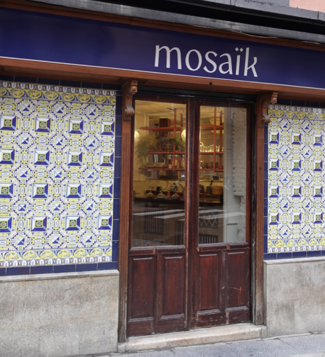 La fachada de Mosaïk Café, sus azulejos azules y amarillos y su puerta de madera, Calle de Apodaca en Madrid